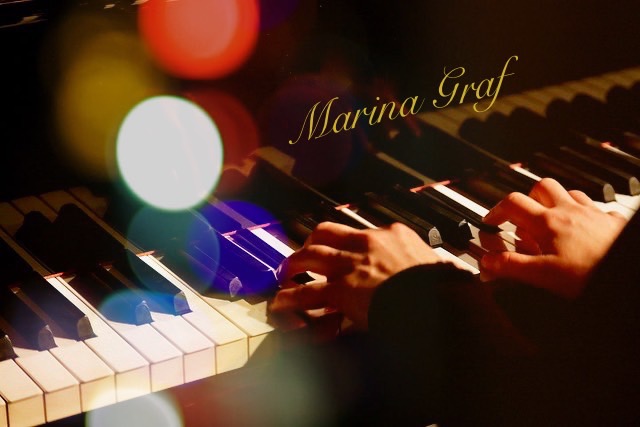 les mains de marina graf sont posées sur un piano à queue jouant du piano. il y a le nom de marina graf de couleur dorée qui est écrit sur le piano. les touches du piano sont de couleurs blanches et noires. un éclairage lumineux et coloré de rouge, blanc, jaune, bleu et vert en cercle sur le côté gauche de la photo.